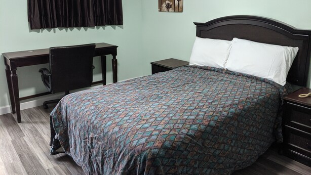 A bedroom with a bed, a desk, a chair, and a nightstand. - Laurel Notch Motel (Bordentown)