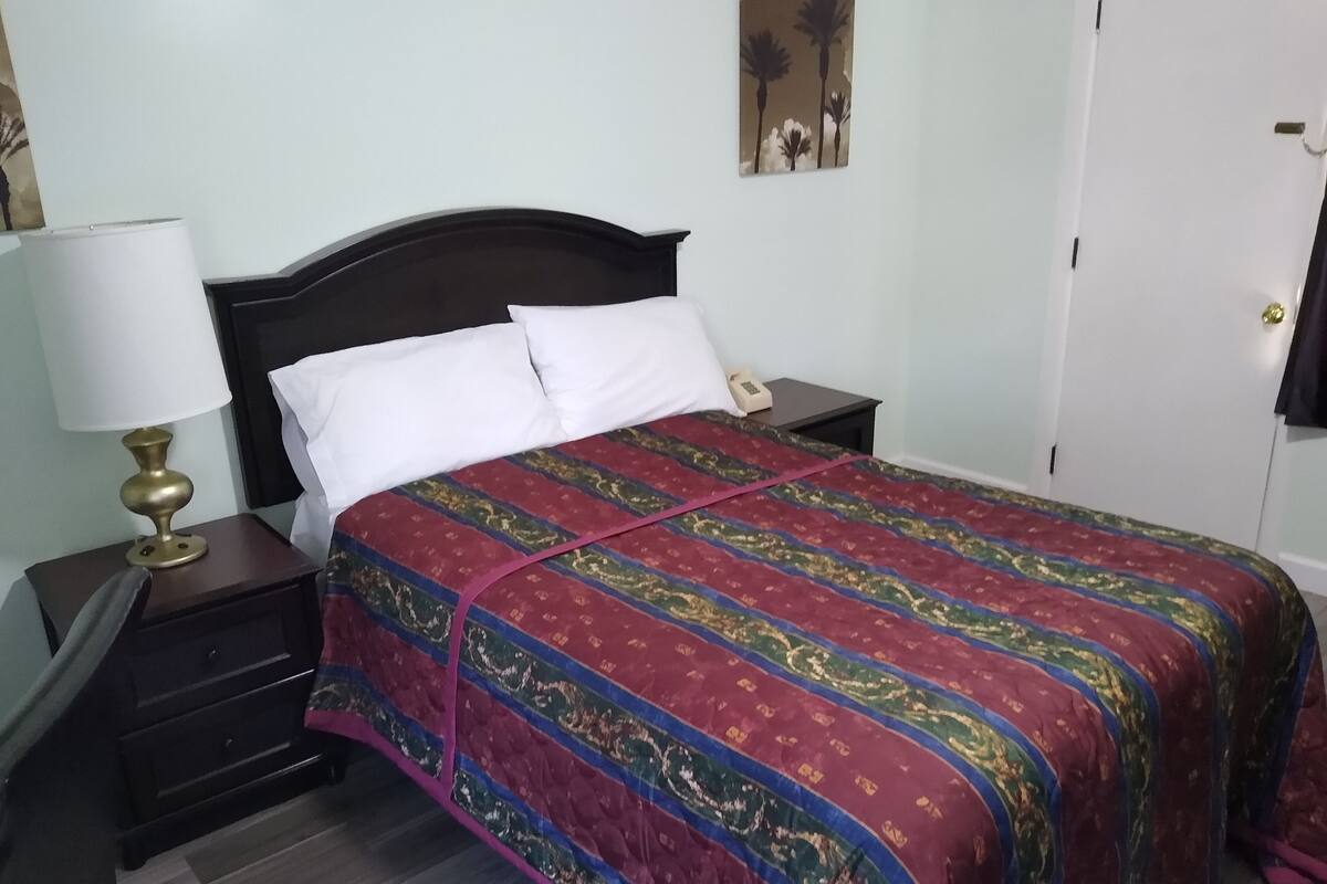 A neatly made bed with a patterned bedspread, a bedside lamp, and a nightstand with a phone.