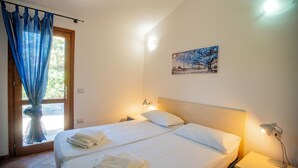 Une chambre avec deux lits, une fenêtre avec des rideaux bleus, un tableau au mur et des lampes de chevet.