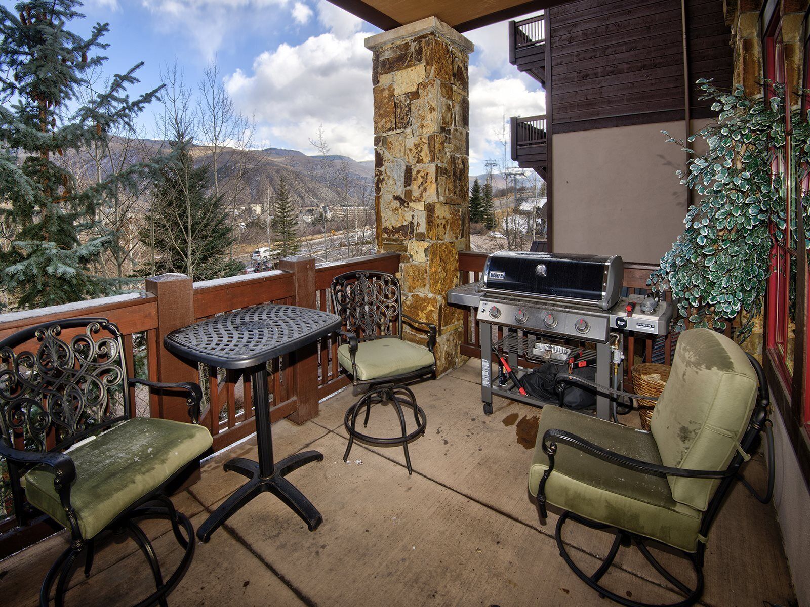 Un balcon avec un pilier en pierre, un barbecue, deux chaises et une table.