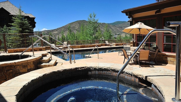 A hot tub with a stone border and metal steps, surrounded by outdoor seating and a mountain view. - Beaver Creek Landing Condo 202 (Avon)