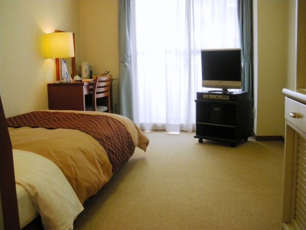 Una habitación de hotel con una cama, un escritorio con silla, un televisor sobre un mueble y una lámpara.