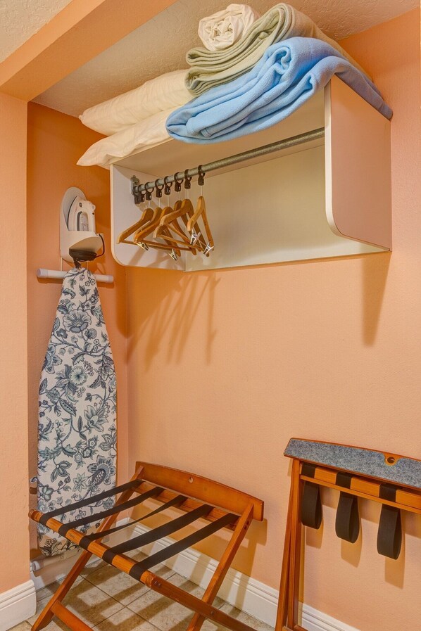 A laundry area with a drying rack, ironing board, and a shelf with folded towels and hangers. - Pelican Pointe Resort (Clearwater Beach)