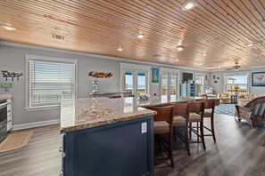 A spacious kitchen with a granite countertop, wooden ceiling, and a view to the living area. - Veronie Villa, Veronie Villa - 100 Steps to the Beach! Great Relaxing Ocean Views (Bolivar Peninsula)
