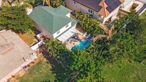 Vista aérea de uma propriedade residencial com piscina, rodeada por vegetação exuberante e uma casa com telhado verde.