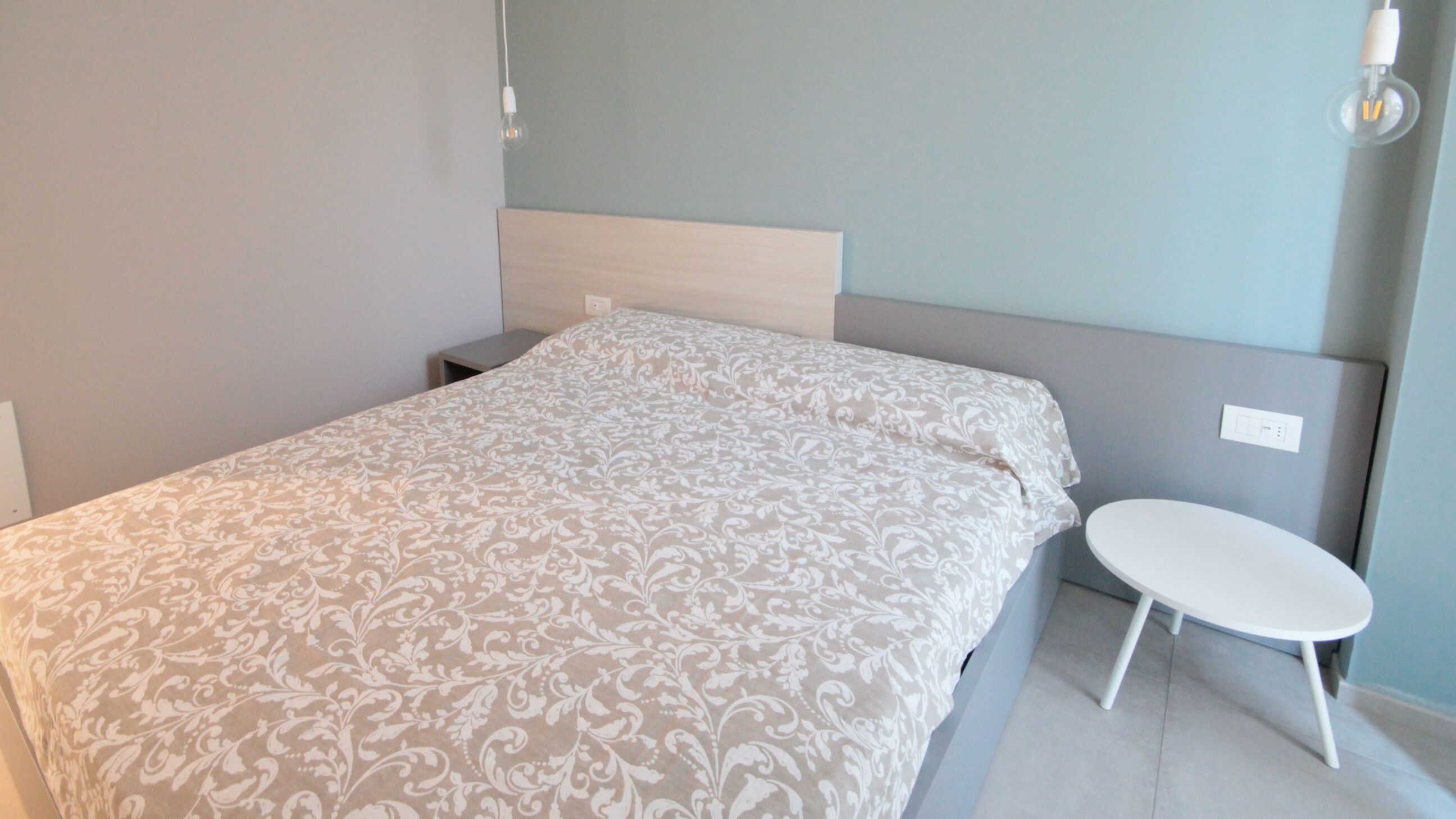 A neatly made bed with a patterned bedspread, a bedside table, and a wall-mounted light fixture.