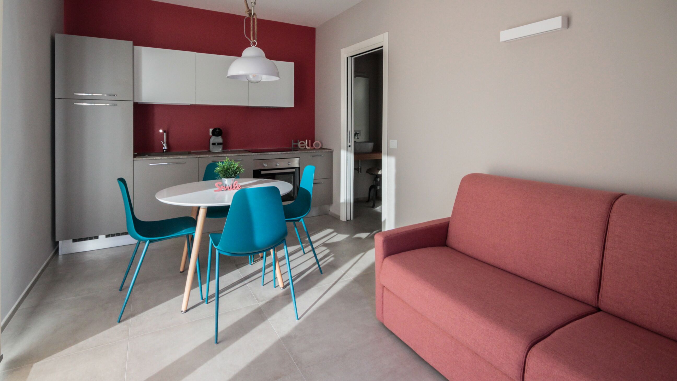 Una cocina moderna con armarios blancos, una pared de acento roja y una zona de comedor con sillas azules y una mesa blanca.