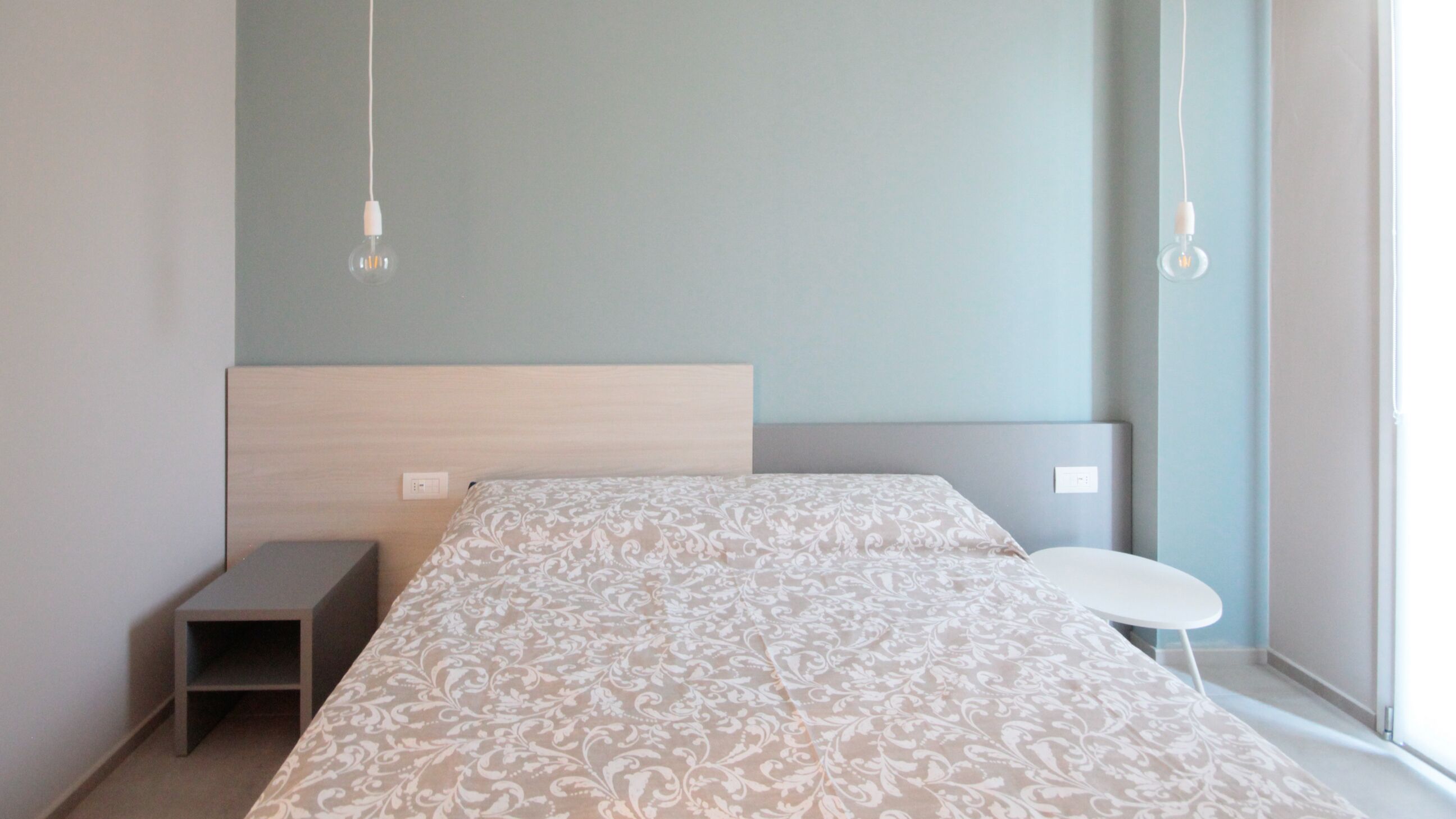 A modern bedroom with a bed, bedside tables, and a small table by the window.