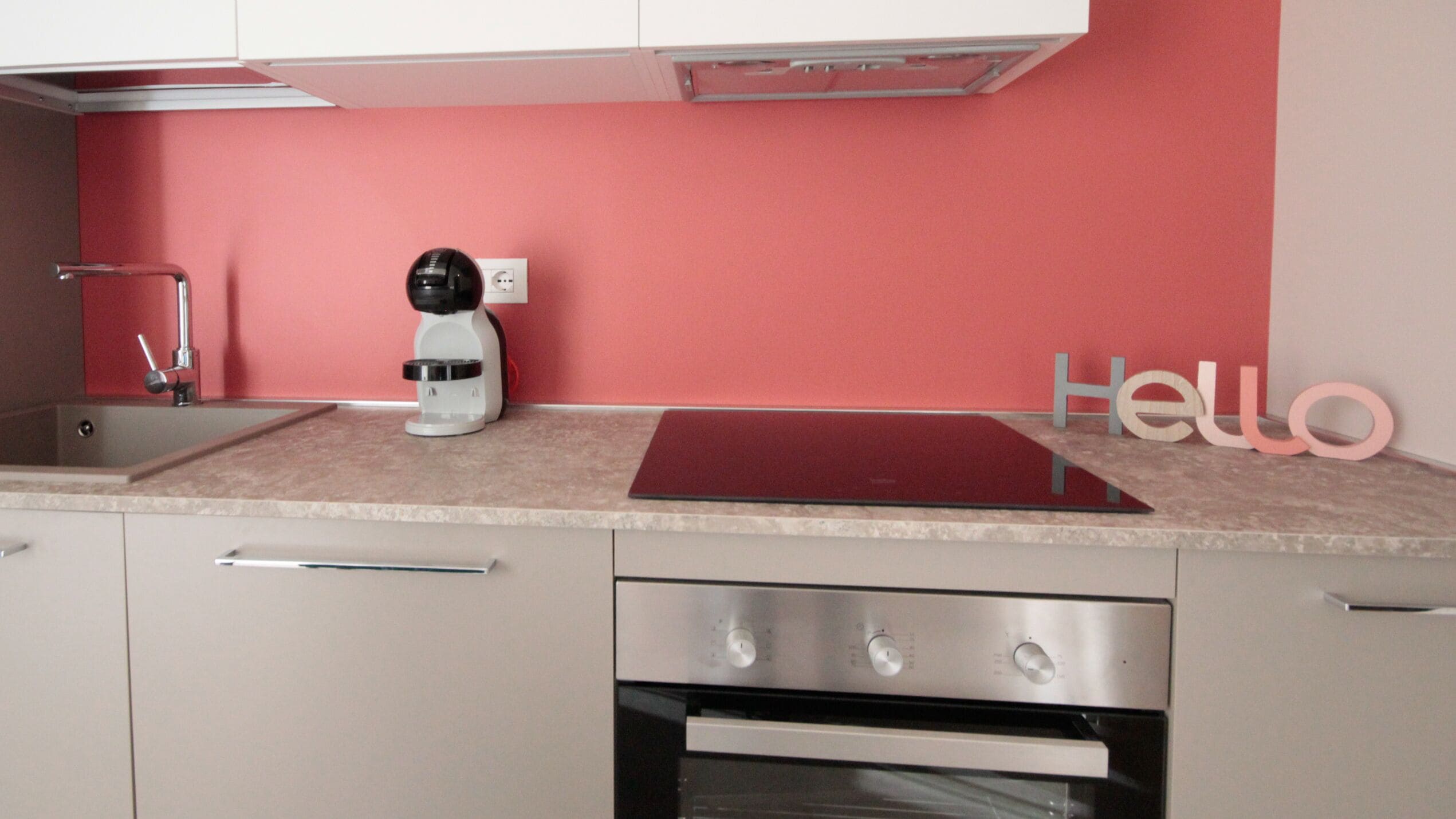 Une cuisine moderne avec un mur de crédence rouge, une machine à café et un panneau indiquant « Bonjour ».