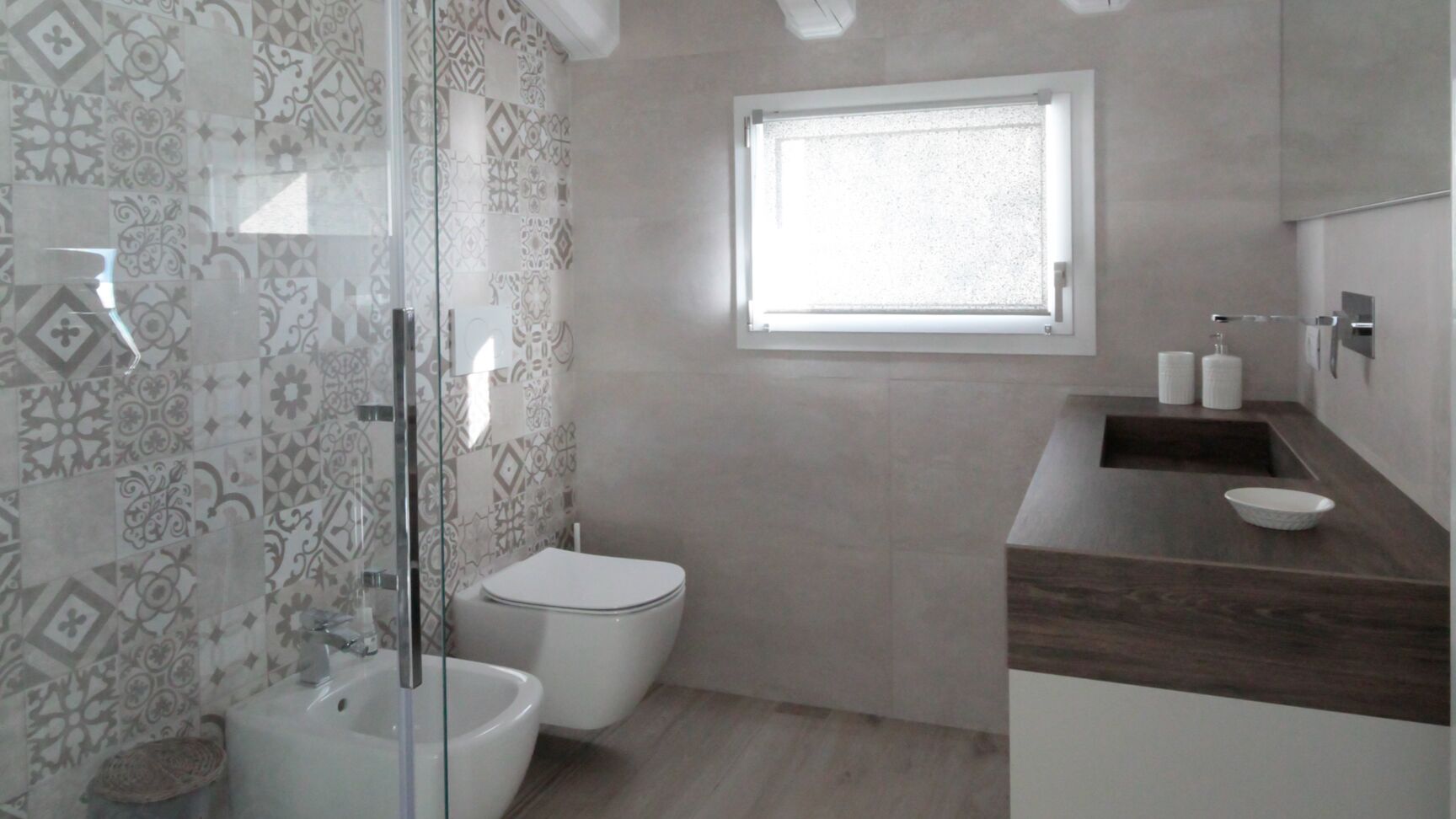 Une salle de bain avec des carreaux décorés, une douche en verre, des toilettes, un lavabo et une fenêtre.