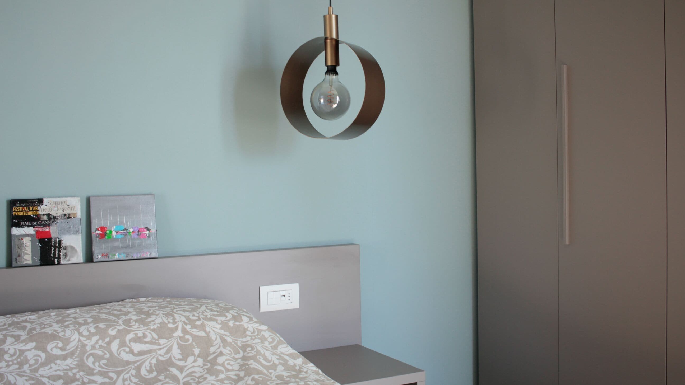 Ein Schlafzimmer mit einem Bett, einem an der Wand befestigten Regal mit Büchern, einer Leuchte und einer Tür.