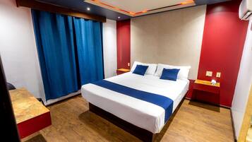 Une chambre d’hôtel moderne avec un grand lit, un plancher en bois, un mur d’accent rouge et un rideau bleu.