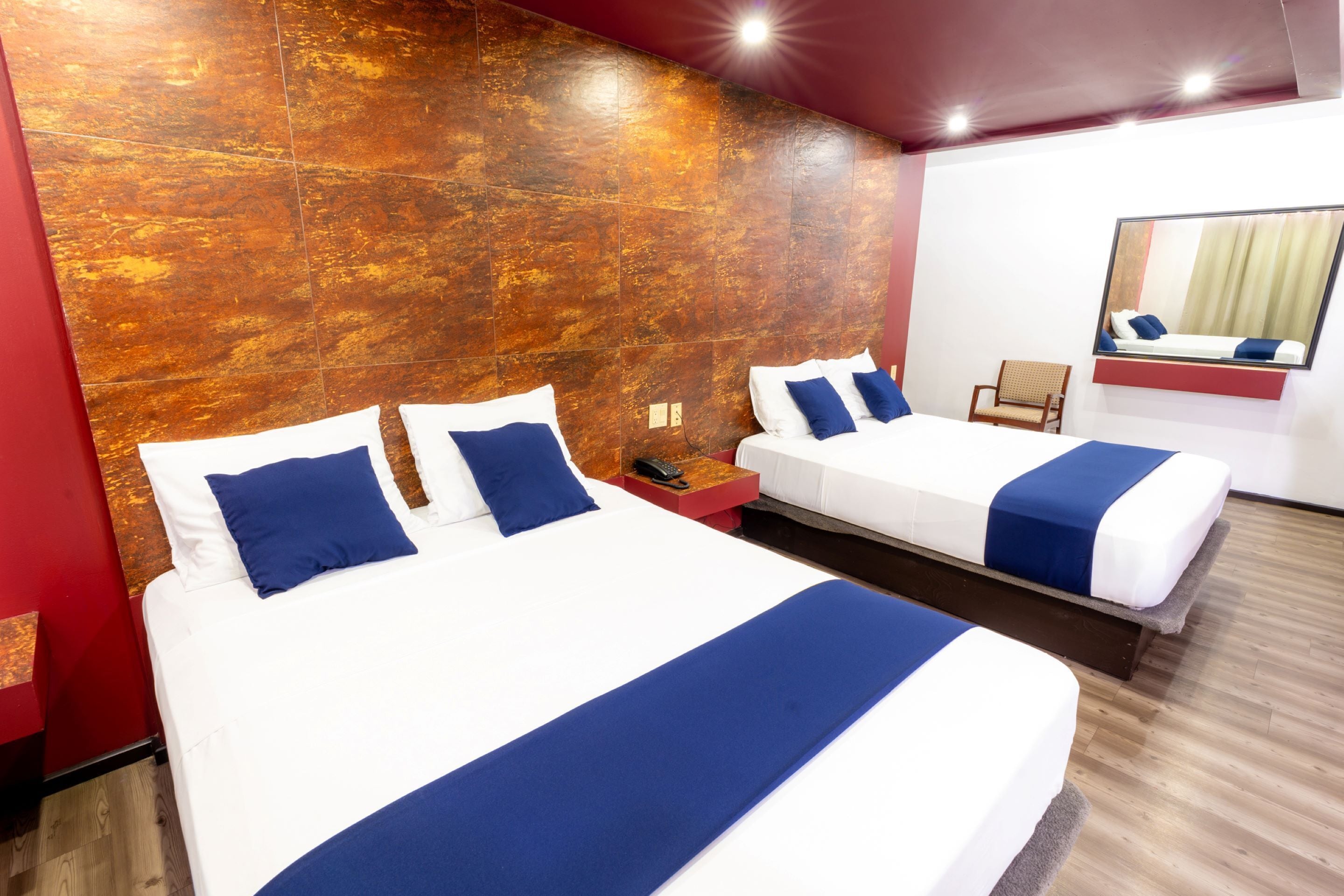 A hotel room with two beds, a wooden accent wall, a mirror, and a wooden floor.