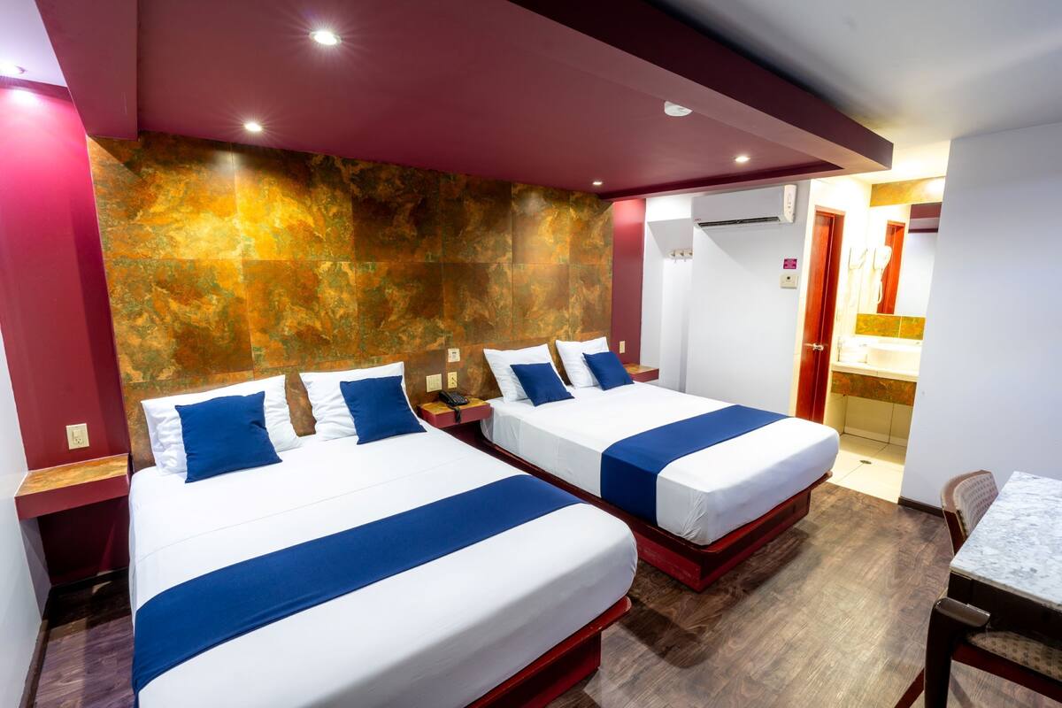 A hotel room with two beds, a wooden floor, and a marble wall.
