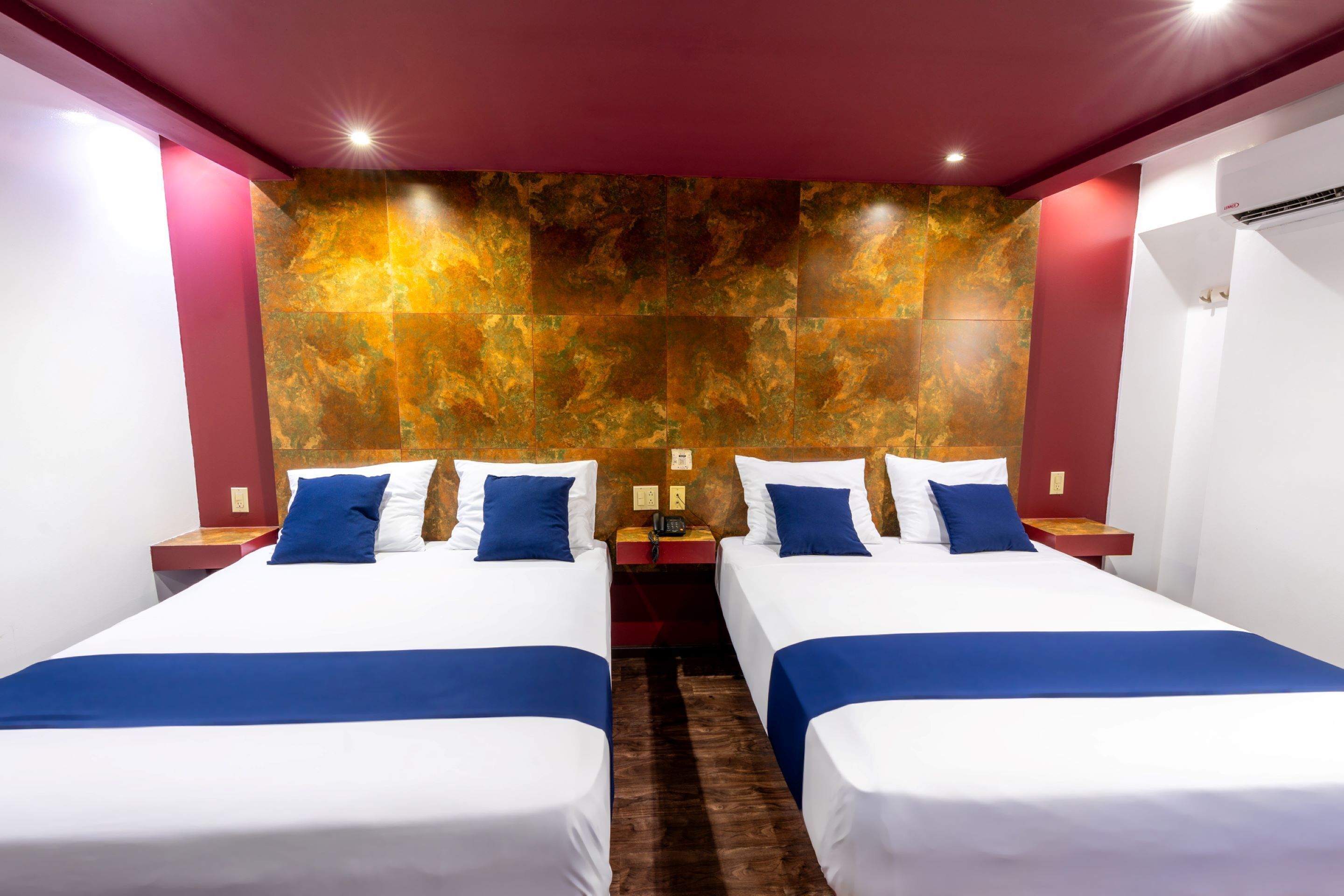 A hotel room with two beds, each with white linens and blue accents, a marble-patterned wall, and a red ceiling.