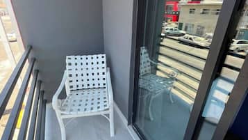 Un balcon avec une chaise blanche, une petite table ronde et une porte vitrée donnant sur la rue.