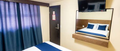 A hotel room with a bed, a mounted TV, and a door with a no-smoking sign.