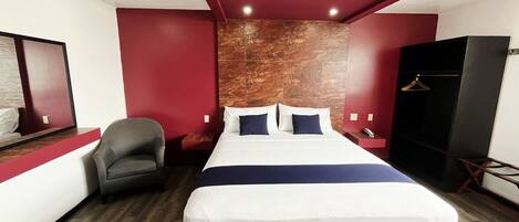 Una habitación de hotel con cama, una silla, armario y espejo.