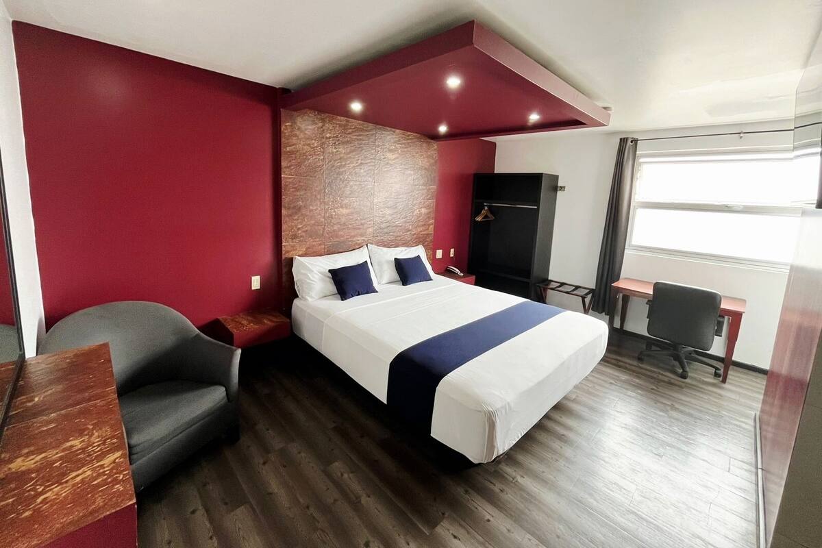 A hotel room with a bed, a desk, a chair, and a wardrobe.