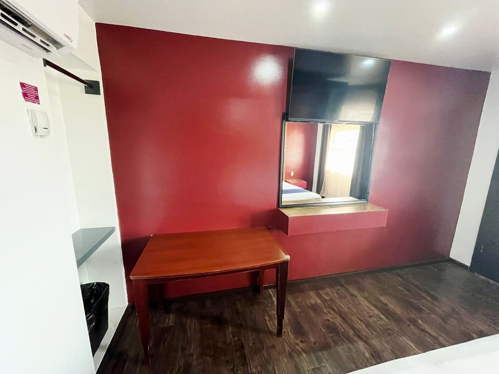 A room with a wooden table, a window with a view, and a red wall.