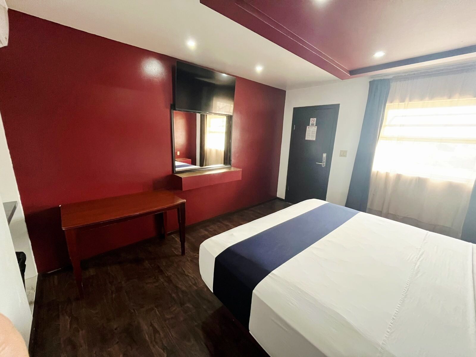 Een hotelkamer met een bed, een bureau, een spiegel, een deur en een raam.