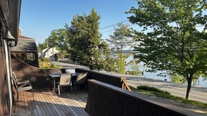 A wooden deck with outdoor seating, overlooking a road and a body of water. - Newfound Lake, Bristol NH Lakefront Cottage (Bristol)