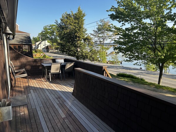 Um deck de madeira com área de estar ao ar livre, com vista para uma estrada e um corpo d'água.
