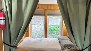 A wooden bunk bed with green curtains, a fire extinguisher, and a window with a view of greenery. - Newfound Lake, Bristol NH Lakefront Cottage (Bristol)