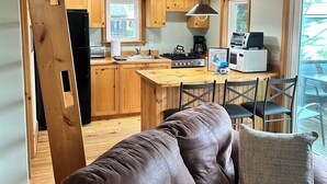 A cozy living area with a brown leather sofa, wooden ceiling, and a kitchen with wooden cabinets and modern appliances. - Newfound Lake, Bristol NH Lakefront Cottage (Bristol)