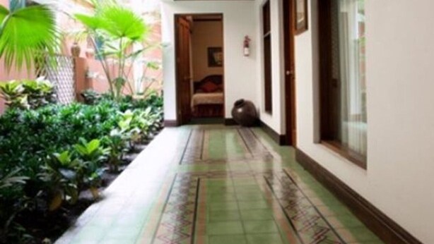 A narrow corridor with tiled flooring, a bed in the background, and potted plants on one side. - Britannia (San José)