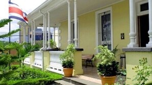 A colonial-style building with a porch, columns, and a flag. - Britannia (San José)