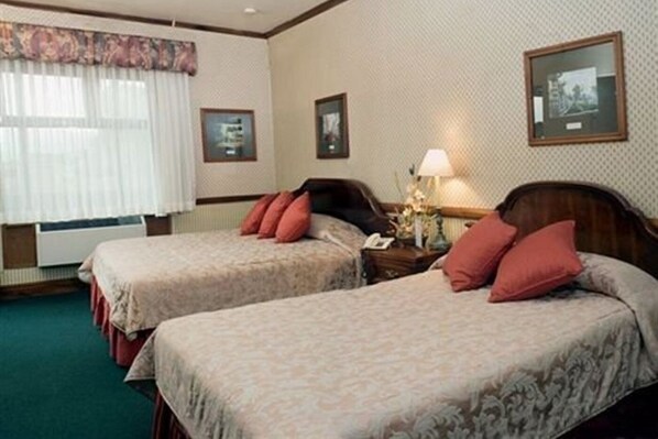 A hotel room with two beds, a nightstand with a lamp, and framed pictures on the wall. - Britannia (San José)