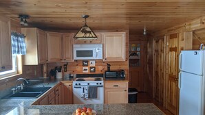 A wooden cabin-style kitchen with granite countertops, a stove, microwave, and a sink. - Knotty Pine Home- 2 Min Walk to Lake and Dock (Rangeley)