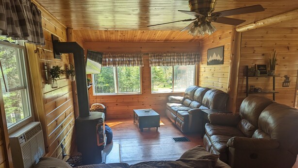 A cozy cabin interior with a sofa, a loveseat, a small table, and a fireplace. - Knotty Pine Home- 2 Min Walk to Lake and Dock (Rangeley)