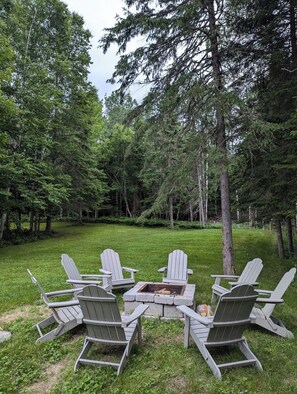 Relax in a serene forest setting with a fire pit and Adirondack chairs.