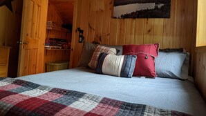A wooden cabin room with a bed, a star decoration, a shelf with books, and a painting of a lake. - Knotty Pine Home- 2 Min Walk to Lake and Dock (Rangeley)
