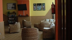 A cozy living area with wicker furniture, a flat-screen TV, and framed artwork on the wall. - La Casita (Antigua)