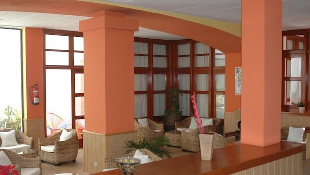 A reception area with wicker furniture, a wooden reception desk, and large windows with curtains. - La Casita (Antigua)