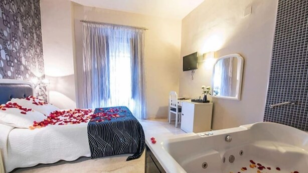 A hotel room with a bed, a sitting area with a chair, a desk, a large bathtub, and a television mounted on the wall. - Las Nieves (Granada)