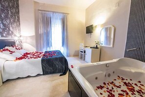 Hotellihuone, jossa on sänky, oleskelualue tuolilla, työpöytä, suuri kylpyamme ja seinälle asennettu televisio.
