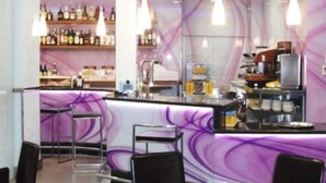 A bar area with a purple-themed bar counter, stools, and a variety of bottles and glasses on shelves. - Las Nieves (Granada)