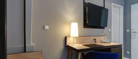 A hotel room with a desk, chair, TV, and a towel on the bed.