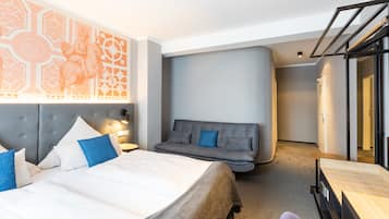 Une chambre d’hôtel moderne avec un grand lit, un canapé gris, un bureau et une armoire.