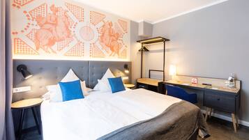 A hotel room with a large bed, a desk, a chair, a lamp, and a wall with a card game design.