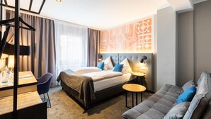Ein modernes Hotelzimmer mit Bett, Sofa, Schreibtisch und einer Wand mit geometrischem Muster.
