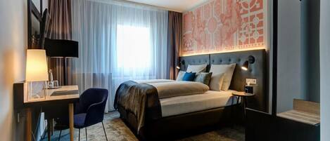 A hotel room with a bed, desk, chair, and a large window with curtains.