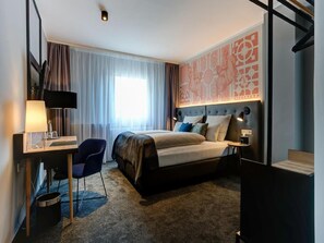 A hotel room with a bed, desk, chair, and a large window with curtains. - YORS Boutique Hotel  (Hannover)