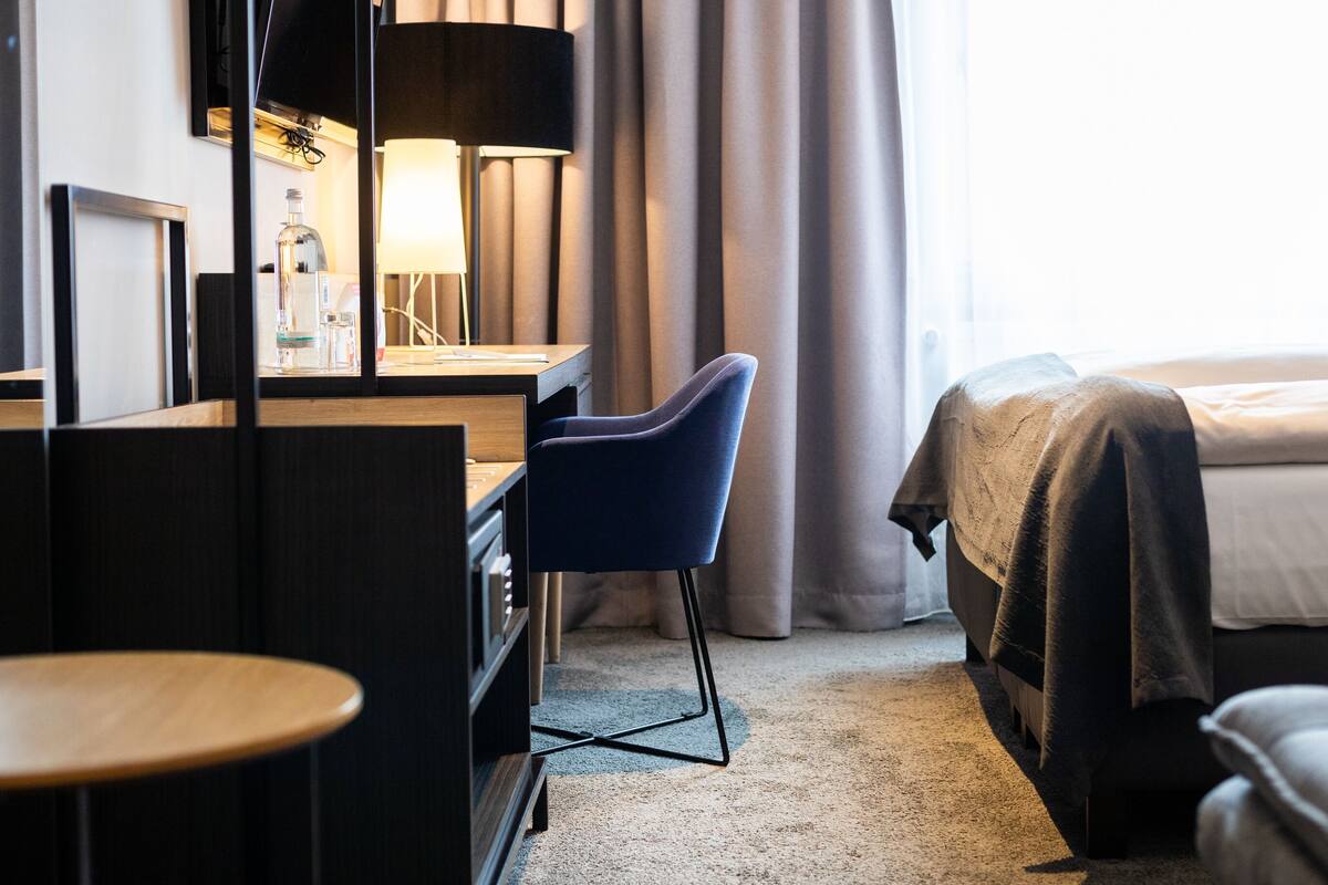 Hotellihuone, jossa on sänky, työpöytä tuolilla, lamppu ja näkymä ulos.
