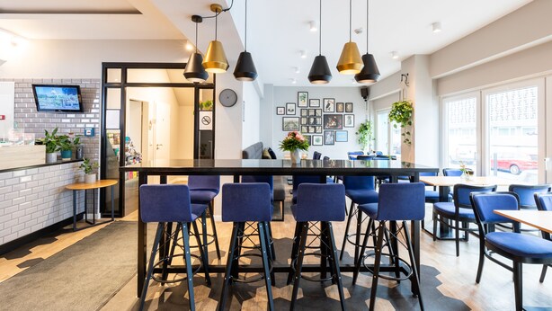Ein stilvoller Barbereich mit einer schwarzen Bar, blauen Barhocker und Pendelleuchten.