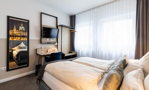 A hotel room with a bed, a desk with a chair, a television, and a large window with curtains. - YORS Boutique Hotel  (Hannover)